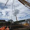 Bauarbeiter arbeiten auf einer Baustelle mithilfe eines Krans an der Einhausung einer Straße.