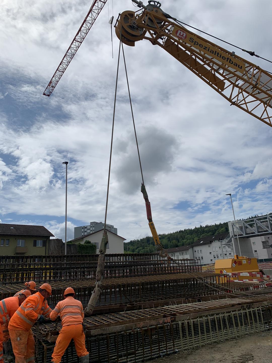 Bauarbeiter arbeiten auf einer Baustelle mithilfe eines Krans an der Einhausung einer Straße.