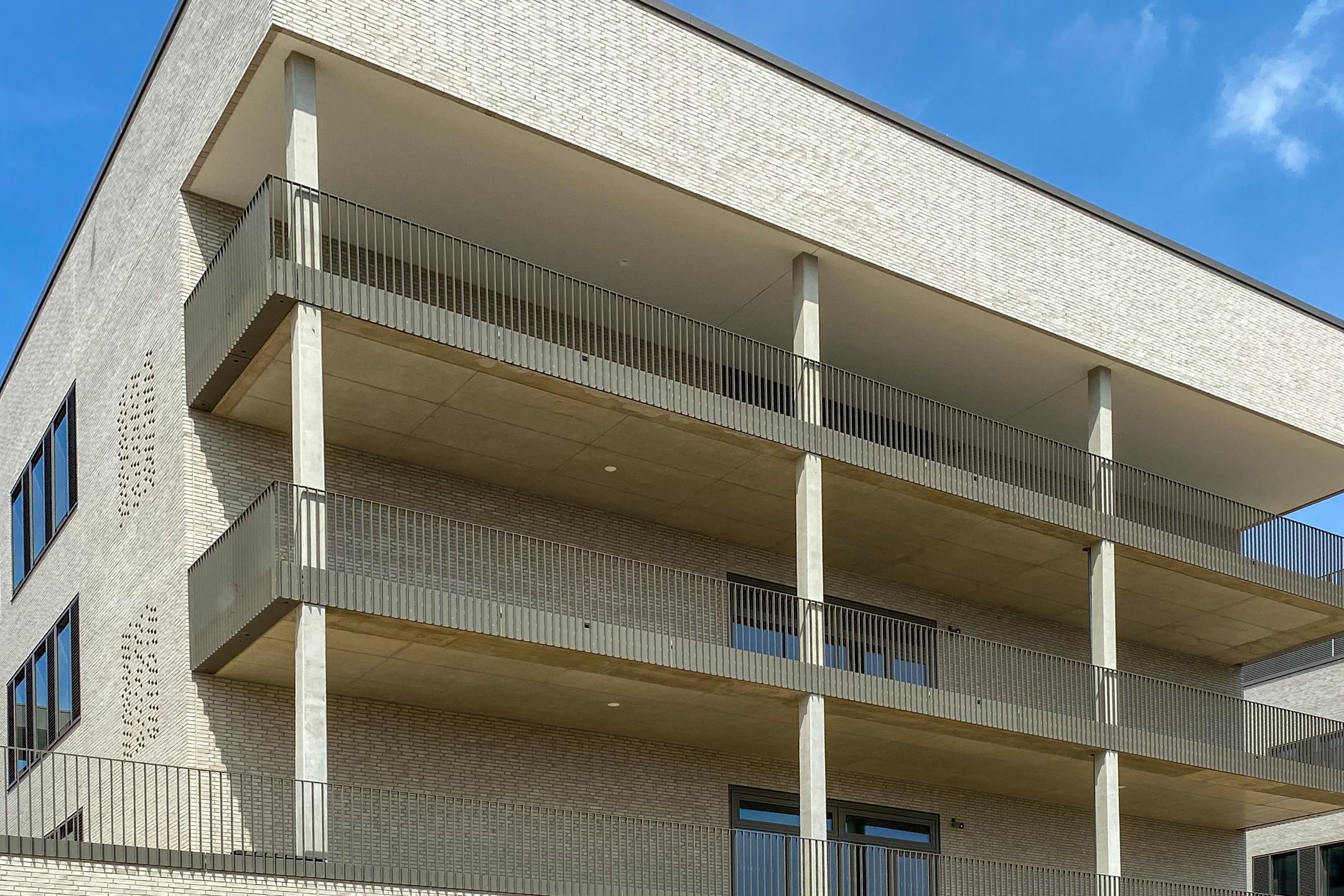 Moderne Fassade mit Klinkersteinen, Balkonen aus Sichtbeton und Metallgeländern, klarer Linienführung und Lochmuster.