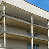 Moderne Fassade mit Klinkersteinen, Balkonen aus Sichtbeton und Metallgeländern, klarer Linienführung und Lochmuster.