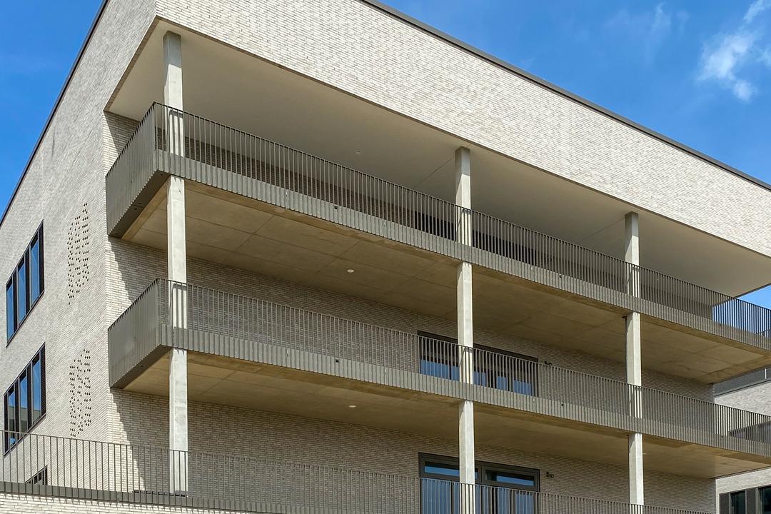 Moderne Fassade mit Klinkersteinen, Balkonen aus Sichtbeton und Metallgeländern, klarer Linienführung und Lochmuster.