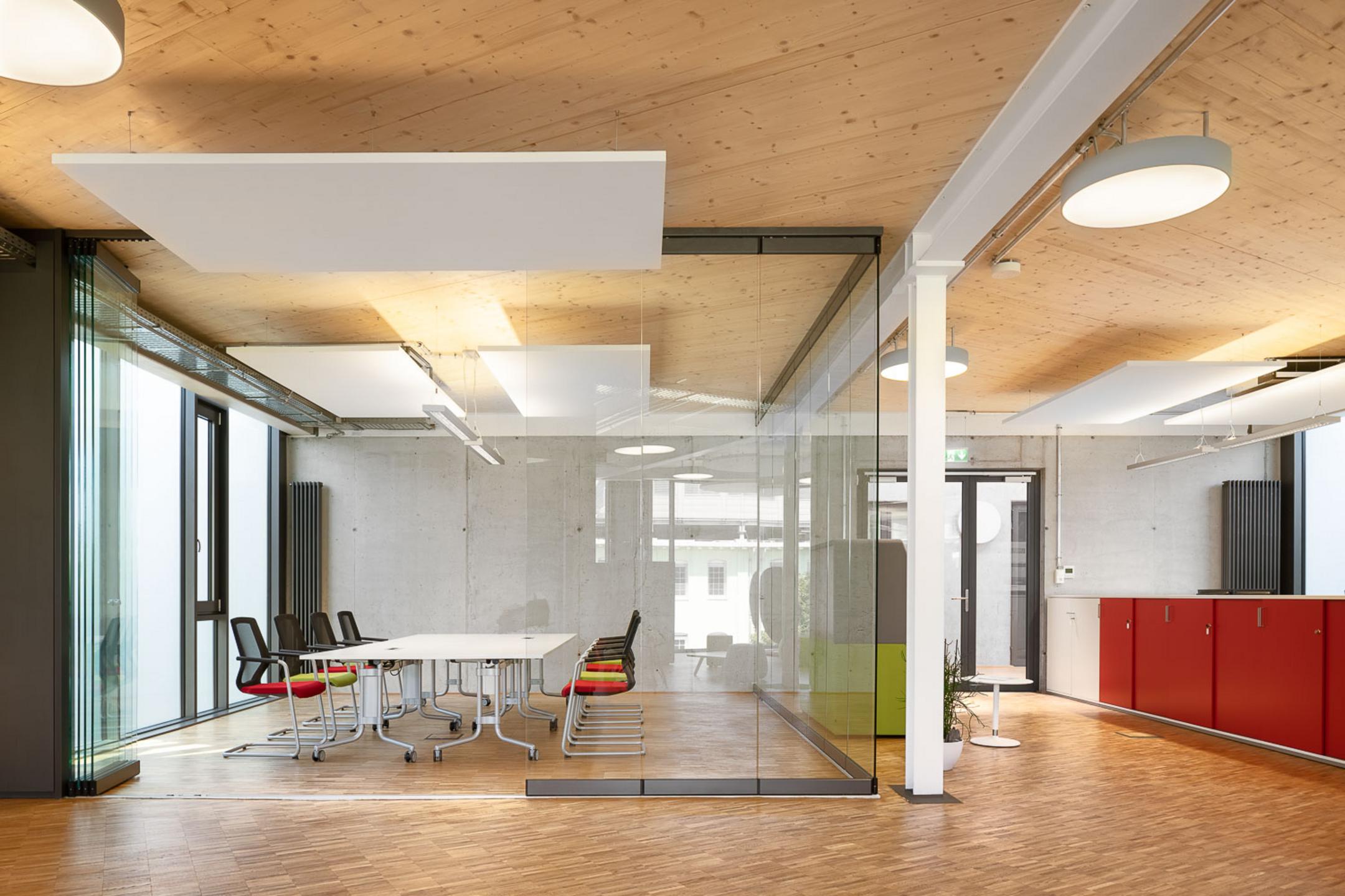 Großes Foyer mit Holzfußboden und Empfangstresen, ein Besprechungsraum mit Tisch und Stühlen ist separat