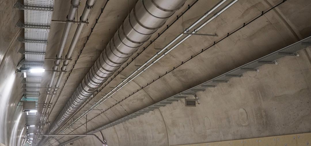 Tunnelbau mit installierten Kabeltrassen, Lüftungsrohren und Leitungen entlang der Betondecke im Infrastrukturbau.
