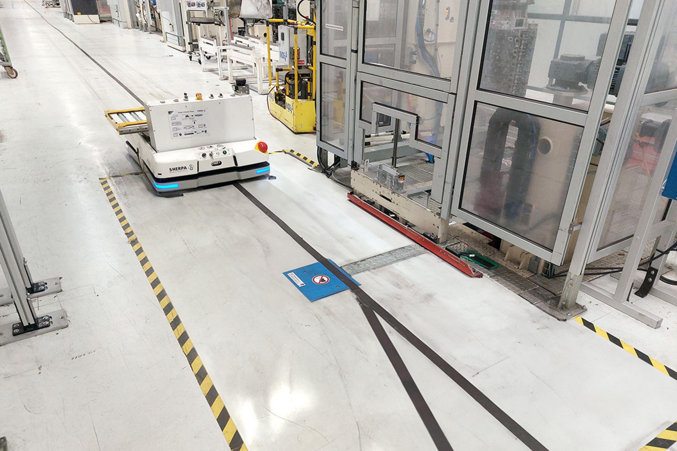 Automatisierter Transportroboter auf einem markierten Industrieboden mit induktiver Ladeeinbaueinheit im Boden