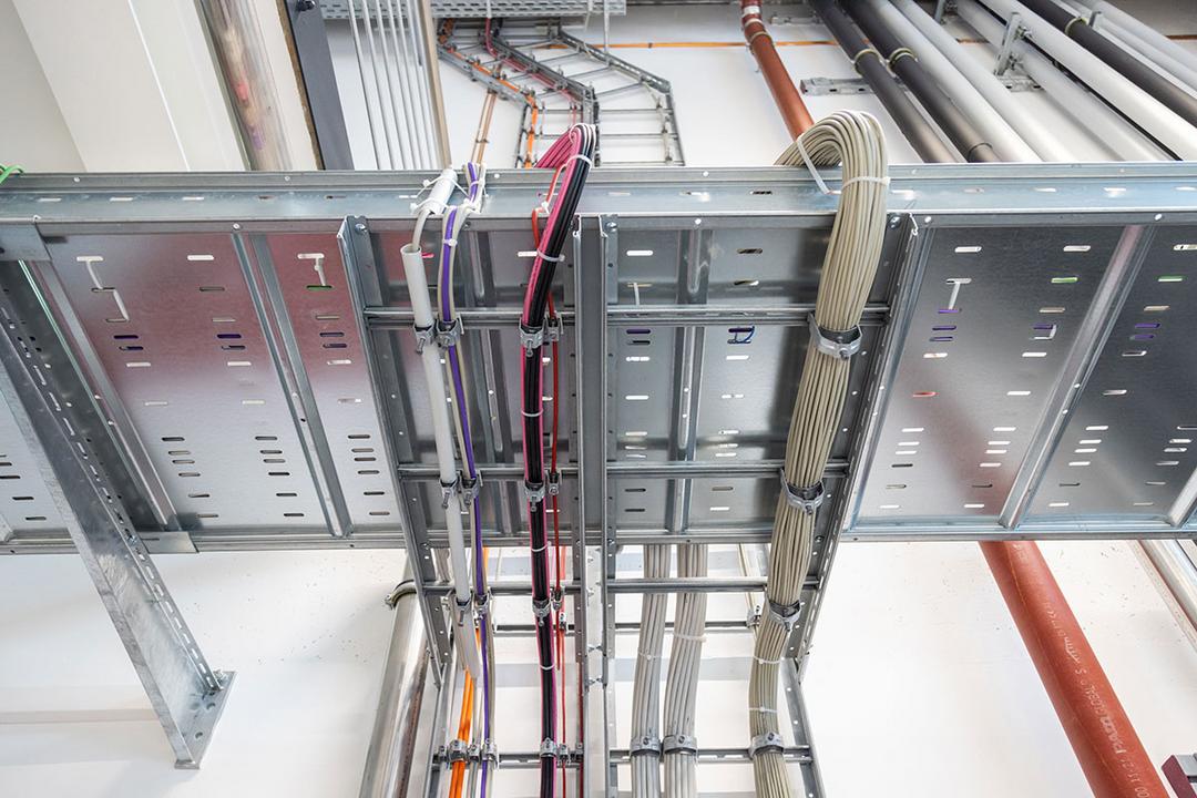 Installierte Weitspannkabelrinnen mit geordnet geführten Strom- und Datenleitungen unter der Hallendecke eines Industriegebäudes.