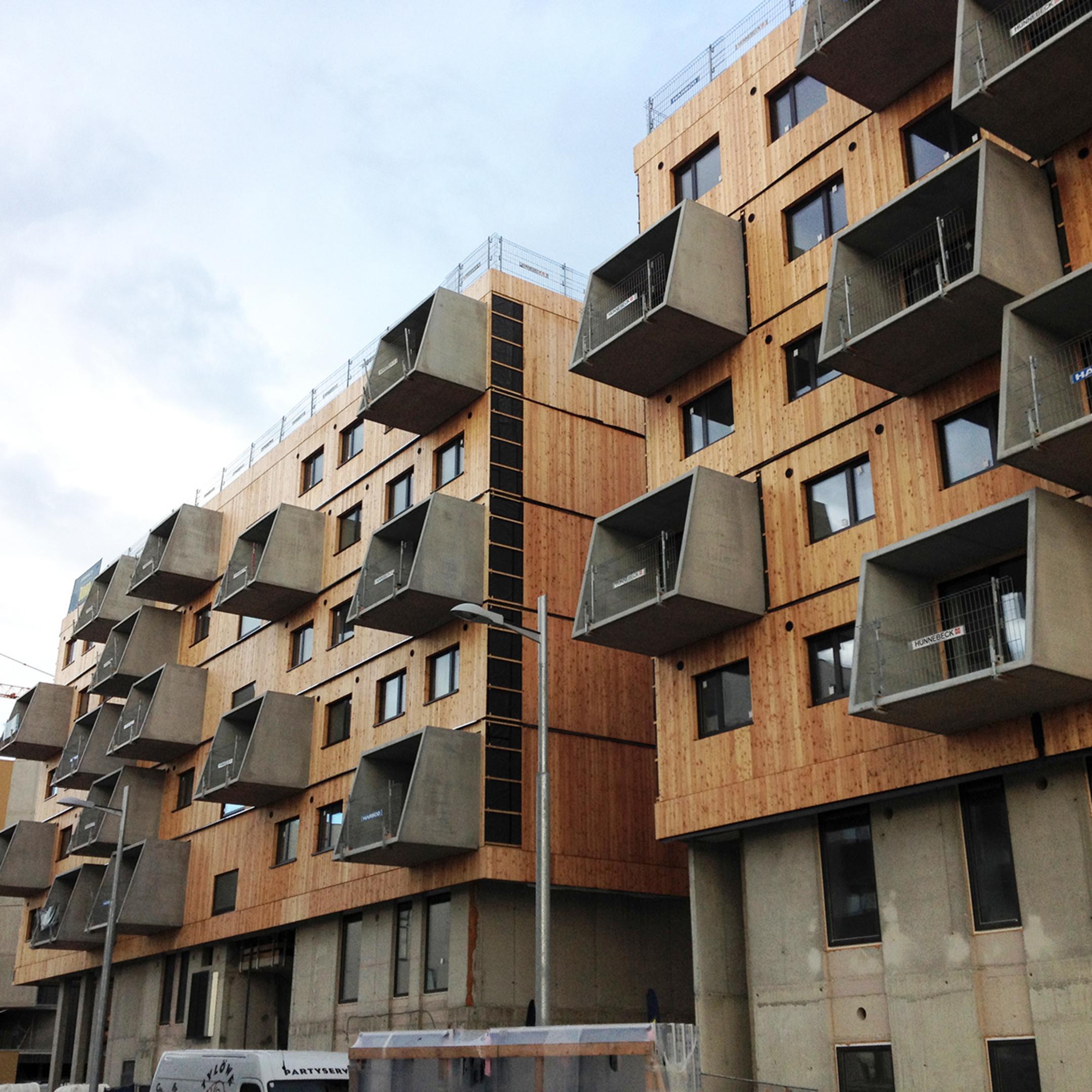 Modernes Wohnhaus mit markanten, eckigen Betonbalkonen und Holzfassade, mehrstöckig mit vielen Fenstern