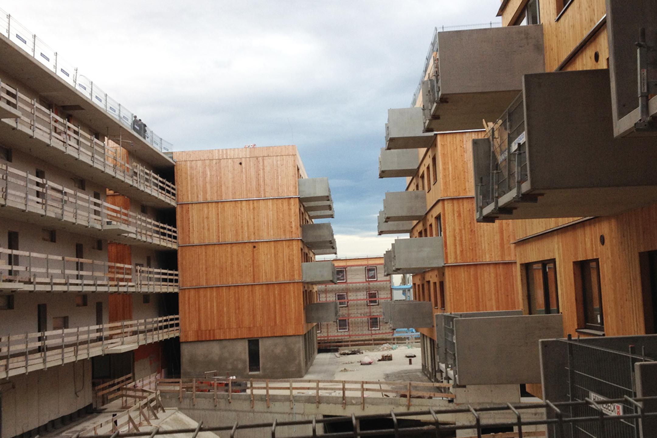 Blick seitlich auf die Baustelle, moderne Wohnhäuser mit Holzfassade und Betonbalkonen