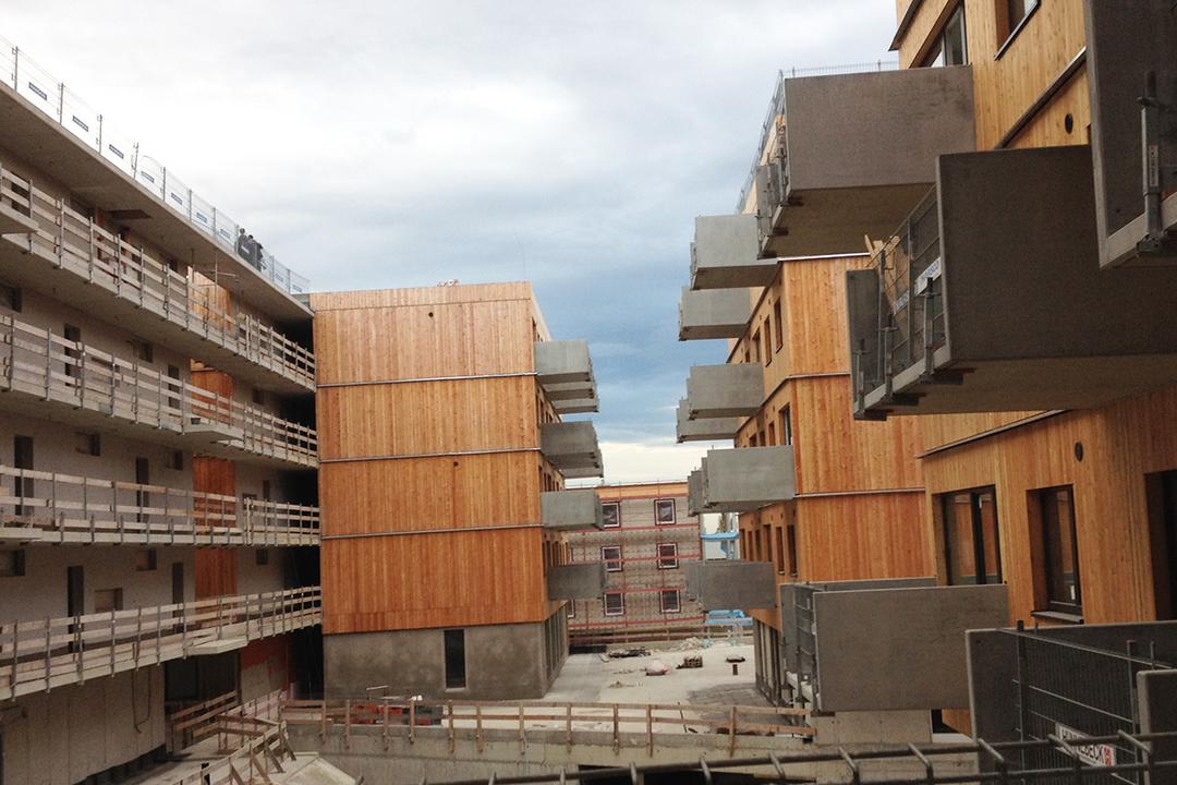 Blick seitlich auf die Baustelle, moderne Wohnhäuser mit Holzfassade und Betonbalkonen