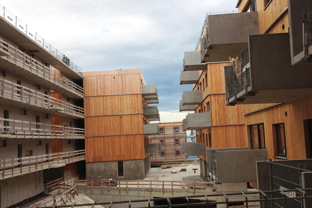 Blick seitlich auf die Baustelle, moderne Wohnhäuser mit Holzfassade und Betonbalkonen