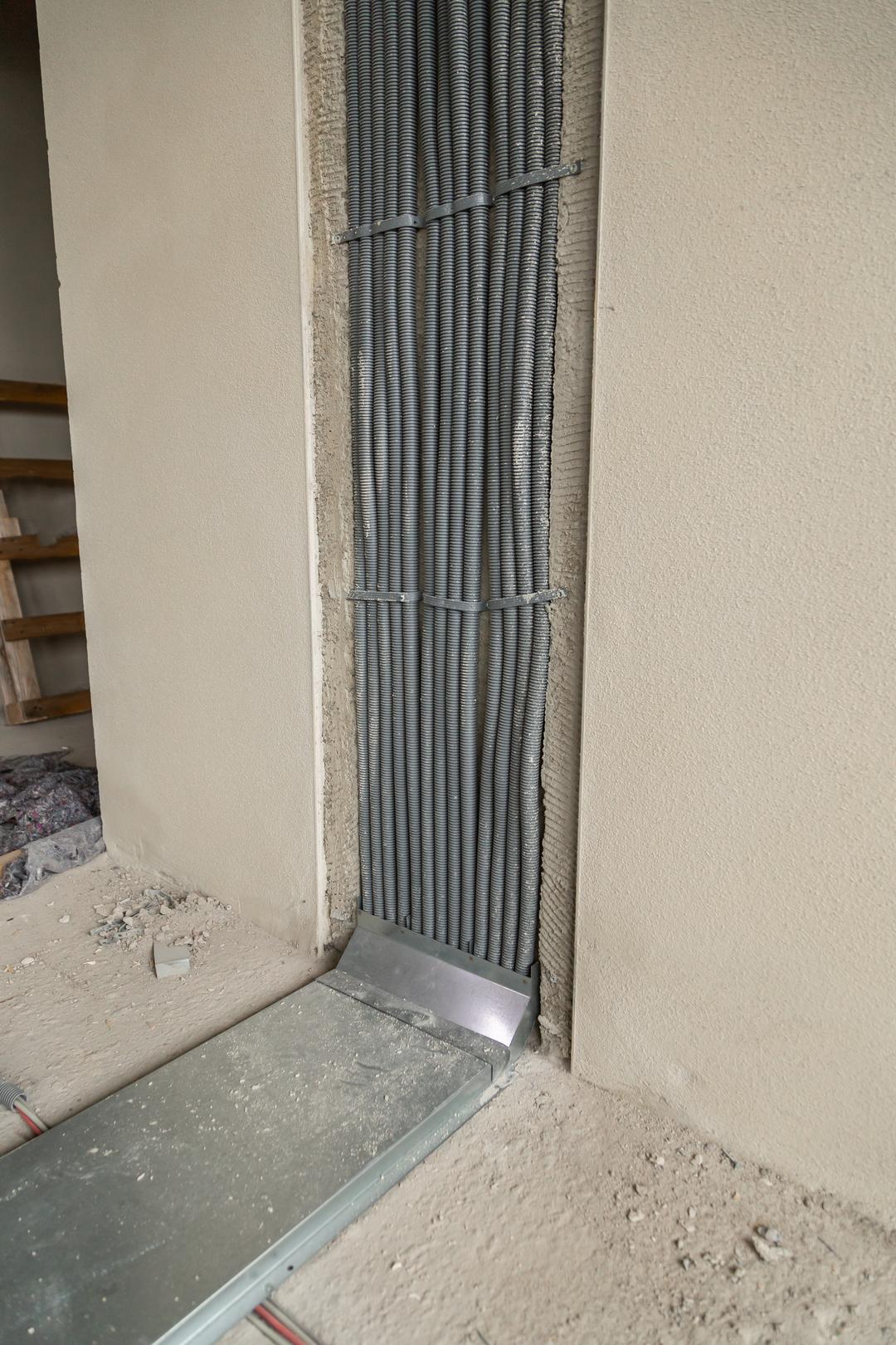 Installierte Kabelschutzrohre in einer Wandnische, verbunden mit einem Bodenkanalsystem auf einer Baustelle.