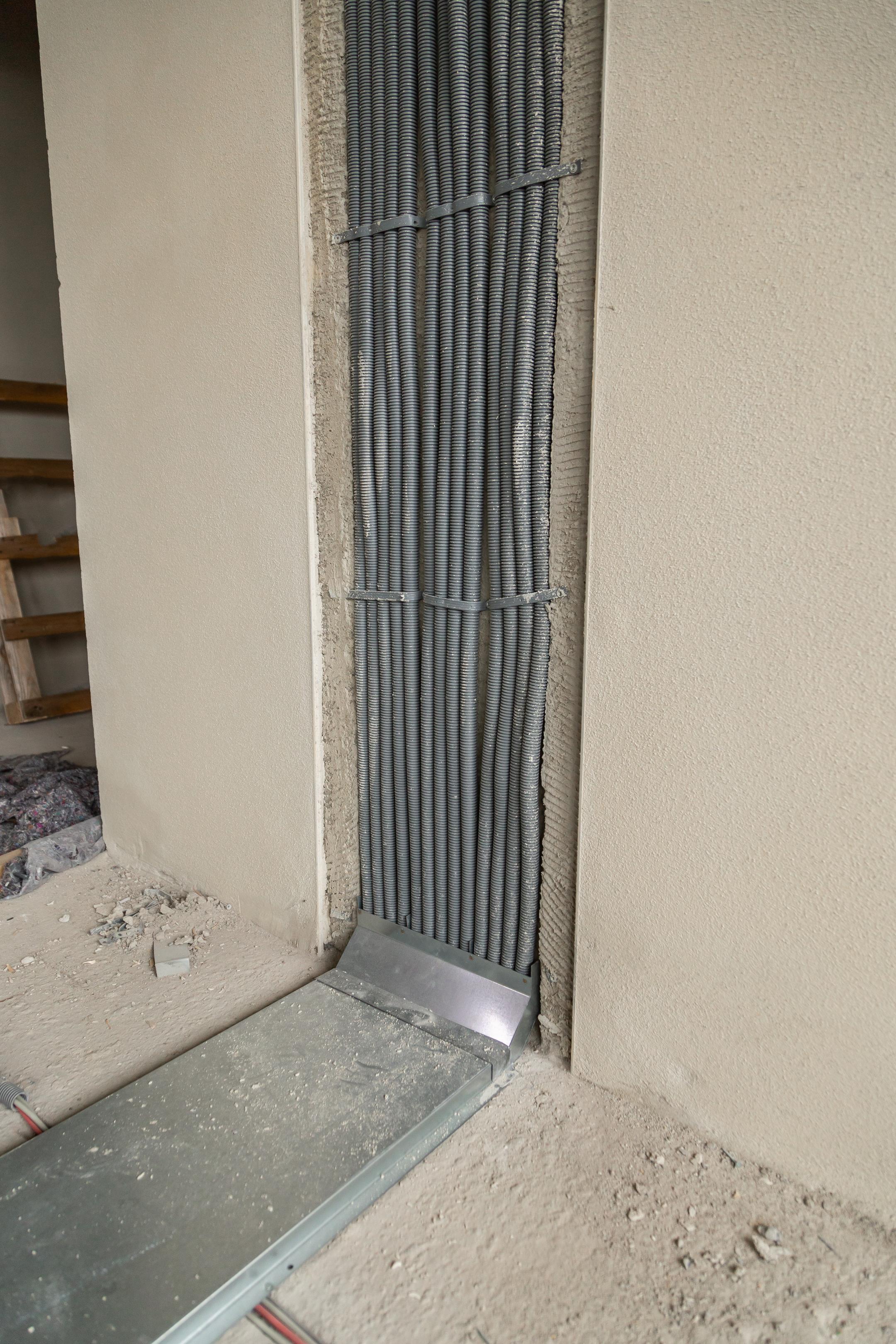 Installierte Kabelschutzrohre in einer Wandnische, verbunden mit einem Bodenkanalsystem auf einer Baustelle.