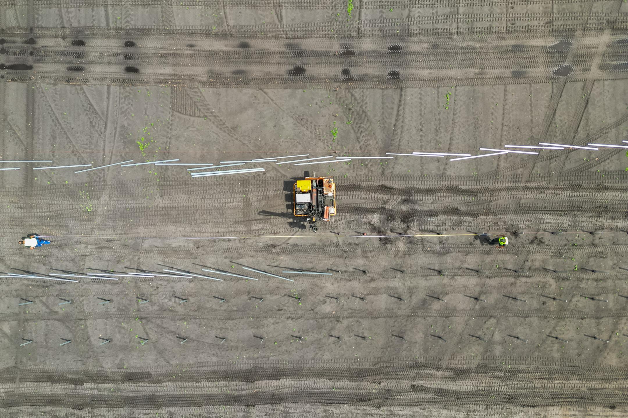 Luftaufnahme einer Baustelle mit Baufahrzeug und Arbeitern beim Setzen von Fundamenten auf vorbereitetem Gelände.