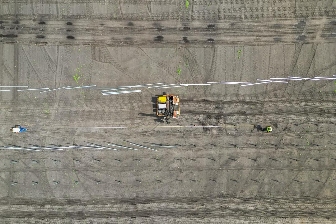 Luftaufnahme einer Baustelle mit Baufahrzeug und Arbeitern beim Setzen von Fundamenten auf vorbereitetem Gelände.
