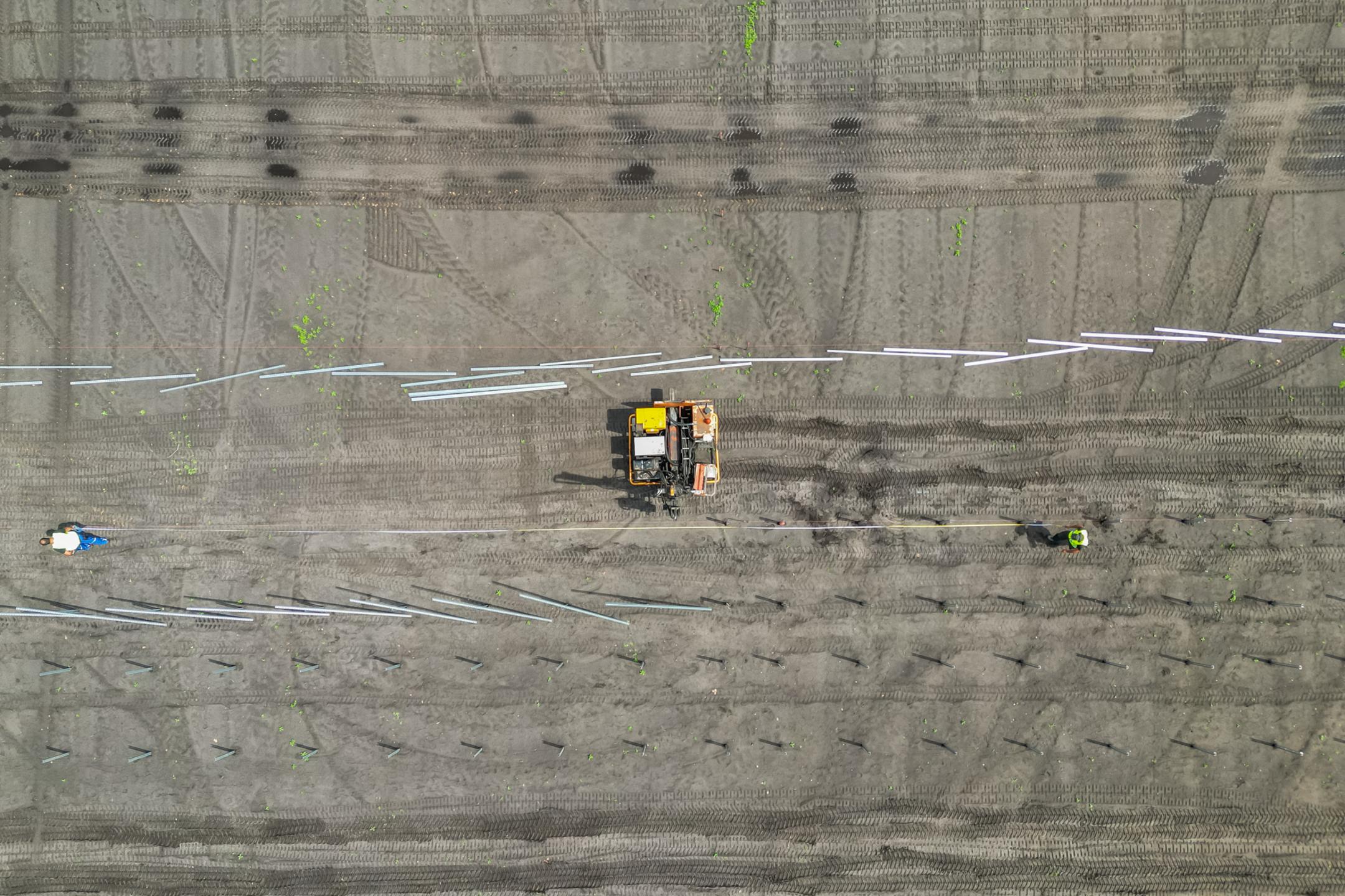 Luftaufnahme einer Baustelle mit Baufahrzeug und Arbeitern beim Setzen von Fundamenten auf vorbereitetem Gelände.