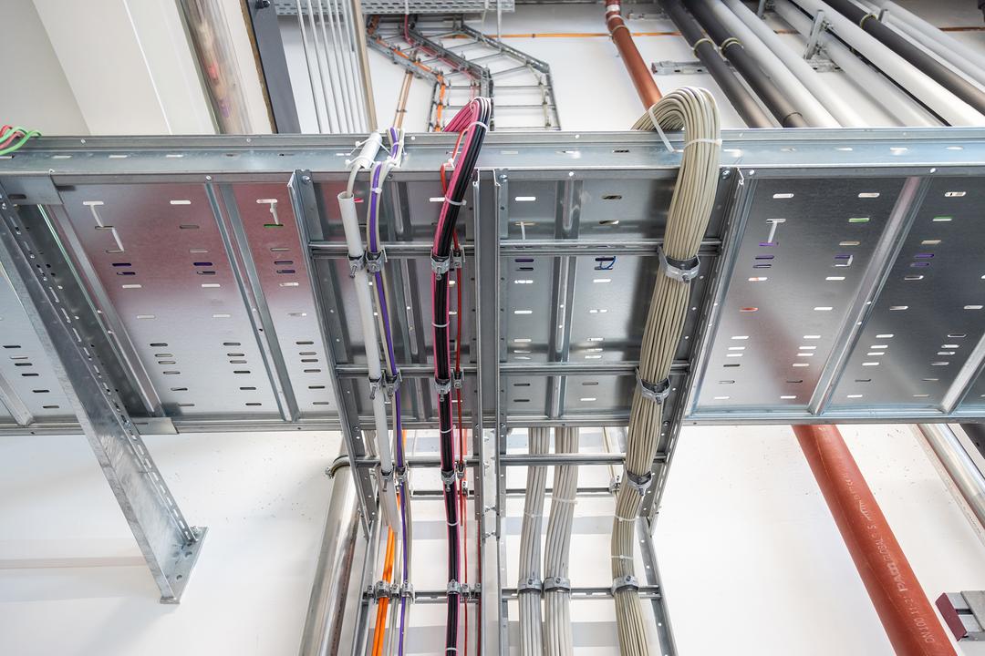 Detailansicht Weitspannkabelrinne und Kabelleiter, die mit mehrfarbigen Kabelsträngen bestückt sind.