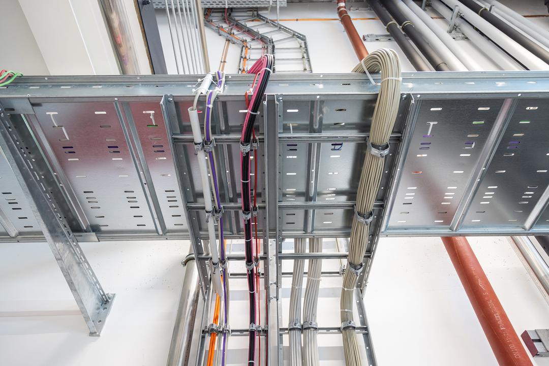 Detailansicht Weitspannkabelrinne und Kabelleiter, die mit mehrfarbigen Kabelsträngen bestückt sind.