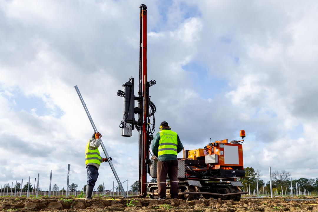 Arbeiter montieren mit Rammmaschine Pfosten für eine Photovoltaik-Freiflächenanlage.