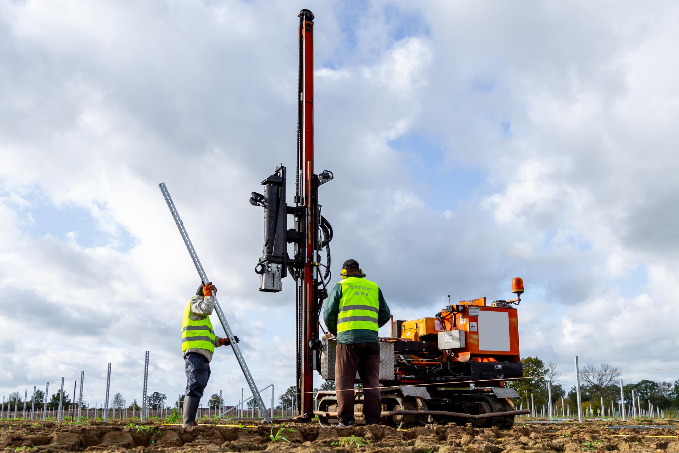 Arbeiter montieren mit Rammmaschine Pfosten für eine Photovoltaik-Freiflächenanlage.