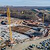 Blick von oben auf die Baustelle, viele Container und Baugerüste sind erkennbar, ringsherum sind Bäume und Felder