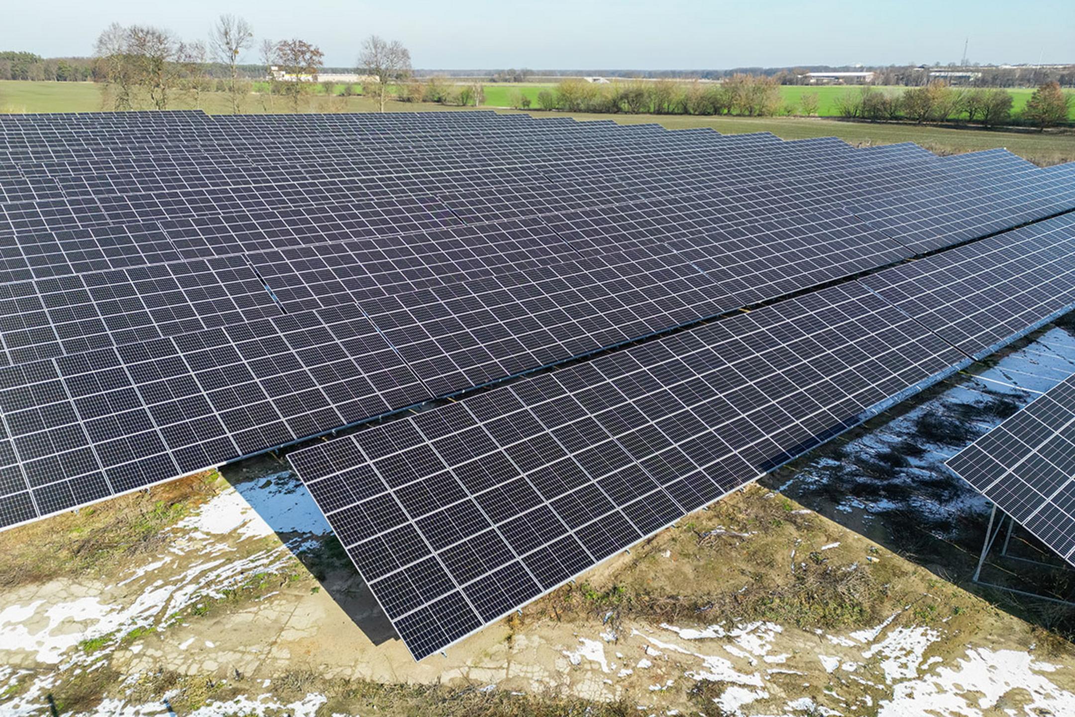 Luftaufnahme eines Solarparks mit angrenzenden Feldern, der Boden ist teilweise von Schnee bedeckt