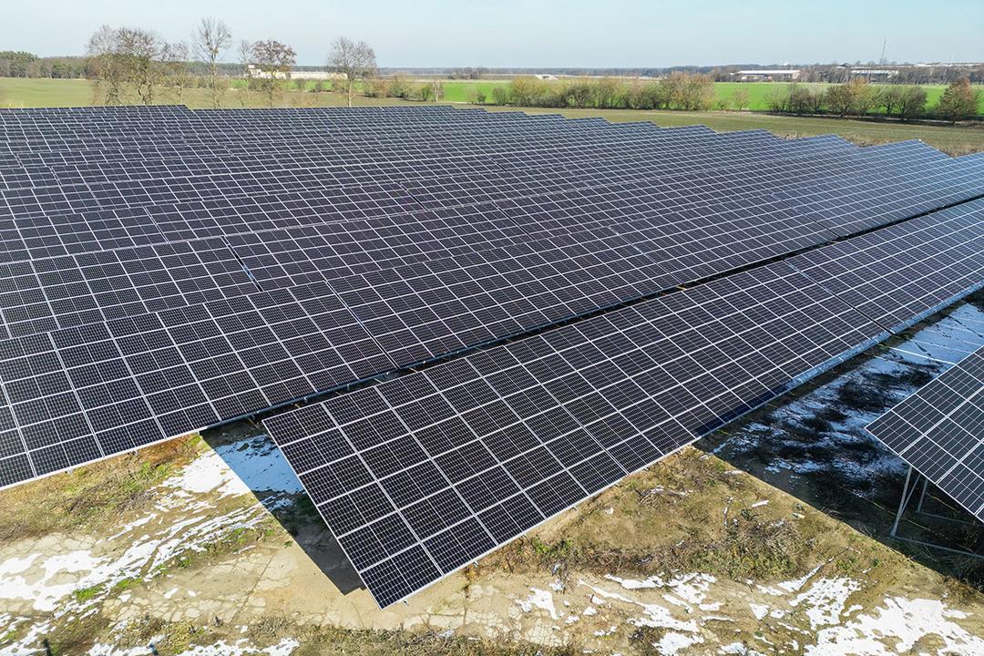 Luftaufnahme eines Solarparks mit angrenzenden Feldern, der Boden ist teilweise von Schnee bedeckt