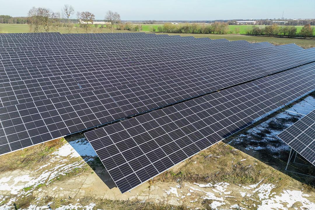 Luftaufnahme eines Solarparks mit angrenzenden Feldern, der Boden ist teilweise von Schnee bedeckt