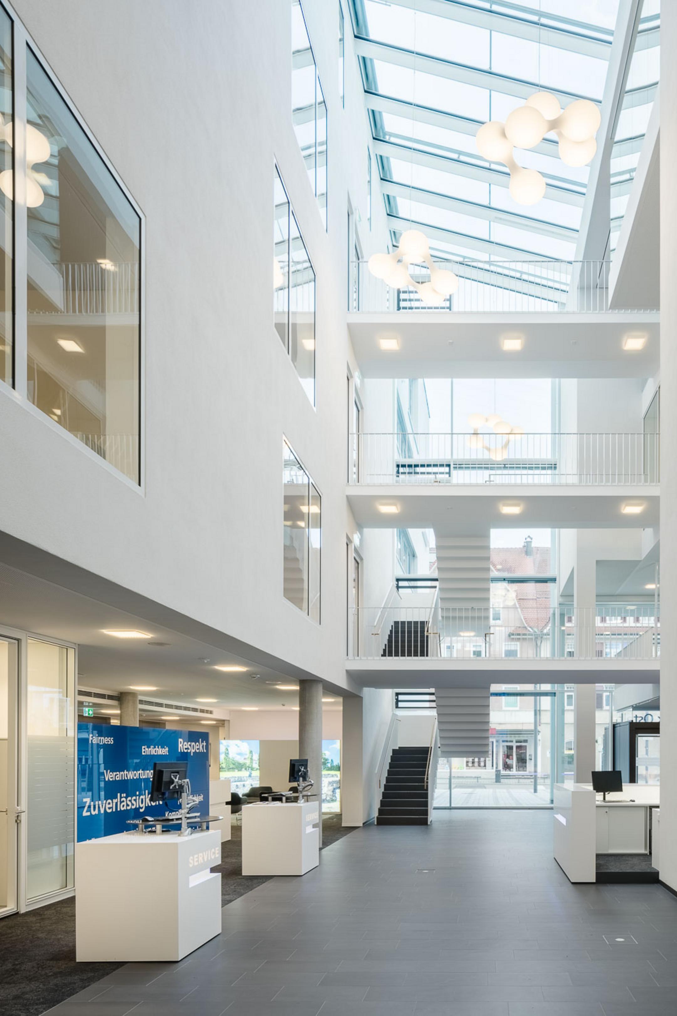 Großer heller Eingangsbereich mit Deckenfenstern, Treppen im Hintergrund und schwarzem Fußboden